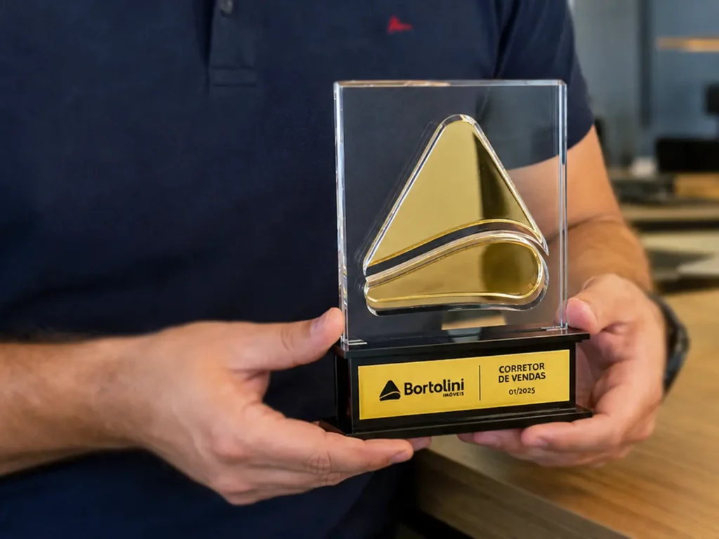 Corretor segurando o troféu com duas mãos, foto exibe apenas o corretor sem rostos.