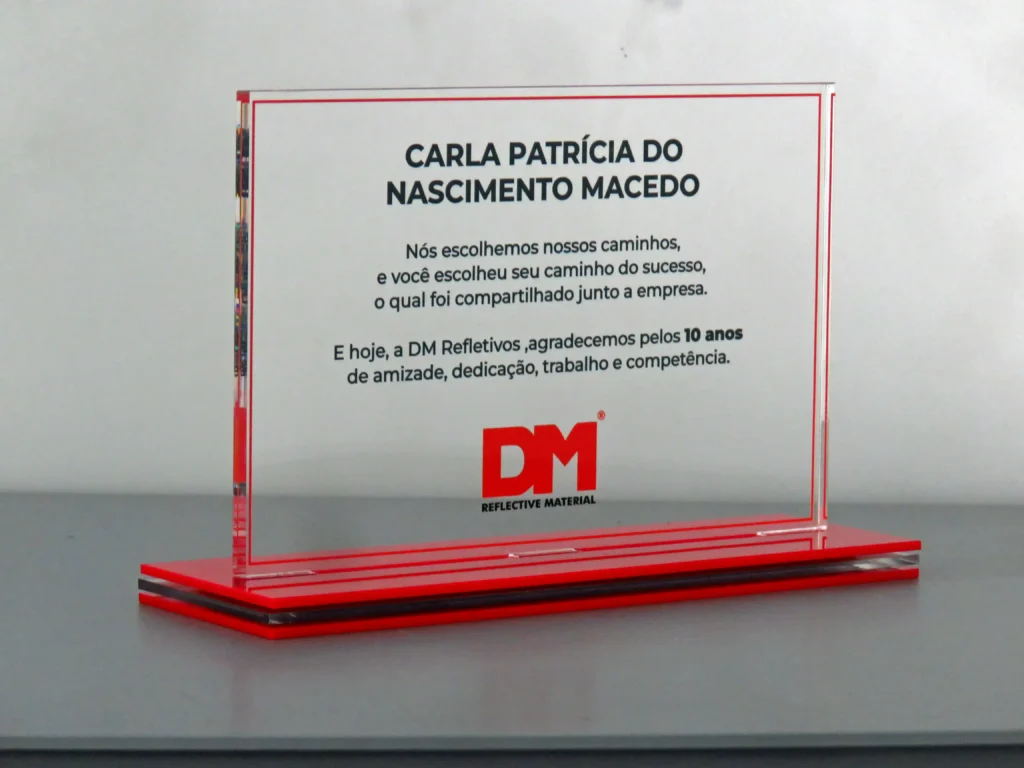 Placa de homenagem, fabricada em acrílico cristal, com base em acrílico vermelho, conforme identidade visual da empresa.