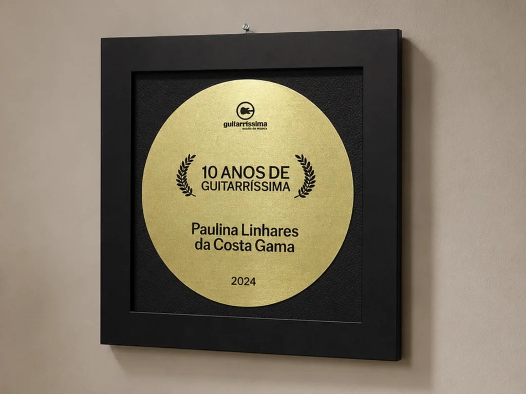 Quadro de homenagem, fabricado em metal latão dourado, com fundo em couro e moldura em madeira preta.